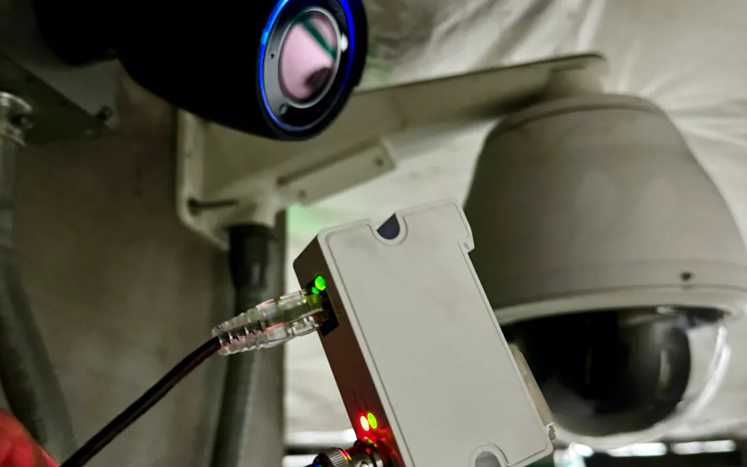 Two dome cameras on a ceiling above a white coax-to-Ethernet converter with an Ethernet cable plugged in.