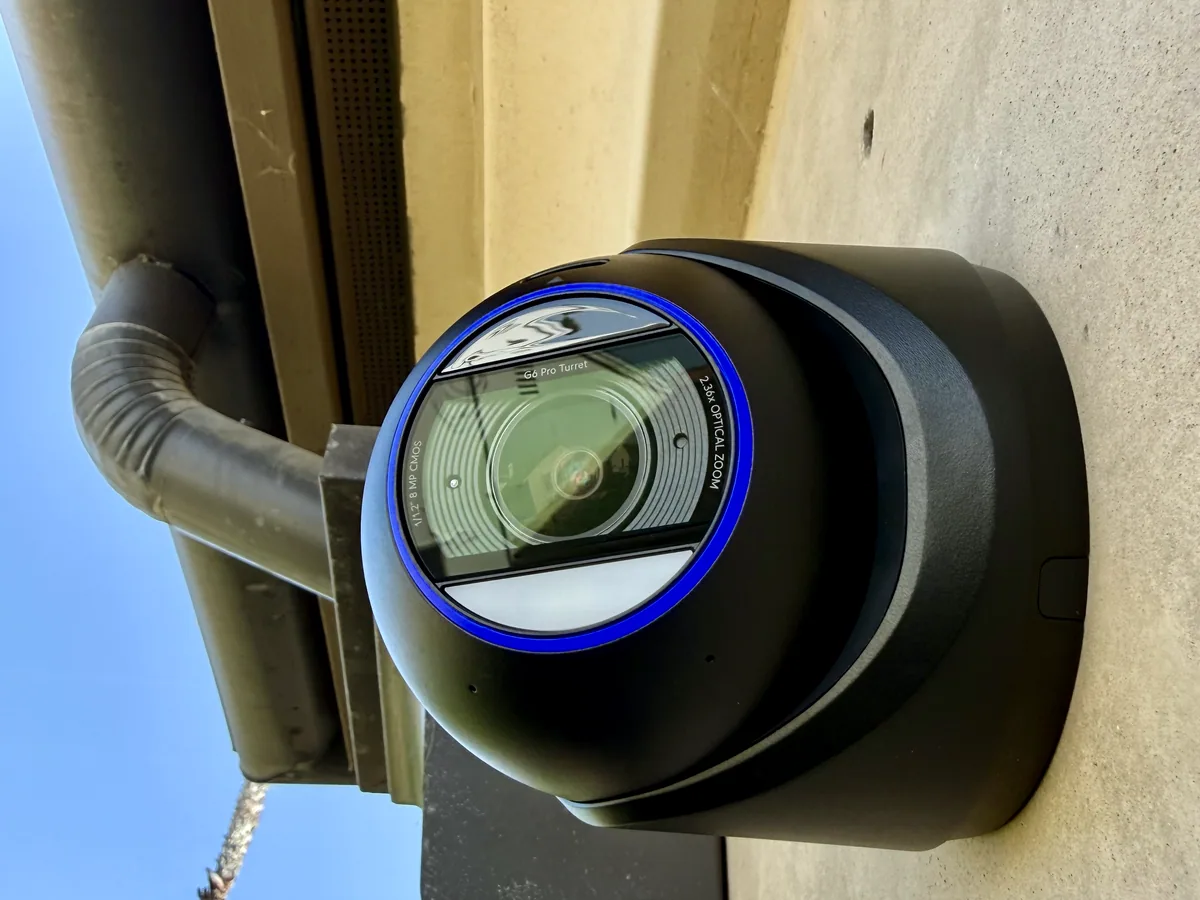 Black UniFi Protect dome camera mounted under the eave of a home, beside a gutter.