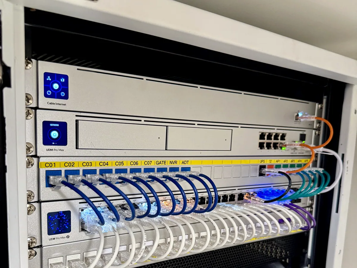 Wall-mounted UniFi rack with silver switches and patch panels, blue patch cables dressed in neat loops.